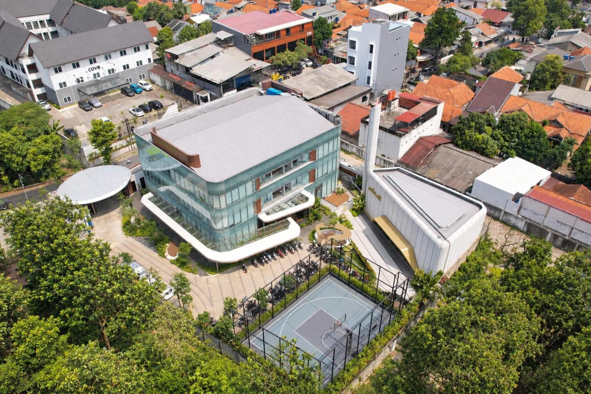 Drone photo of Alien DC HQ: the glass office building, the white mosque with its minaret, the garden courtyard and the fenced basketball court, surrounded by trees