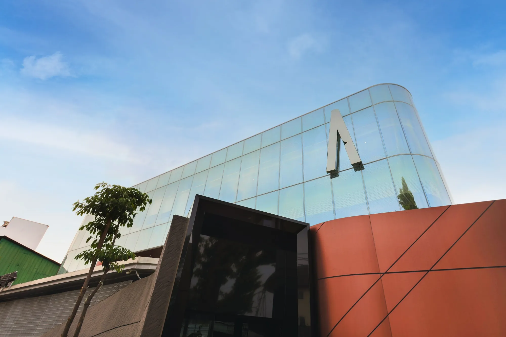 Alien DC HQ: curved glass curtain wall with the Alien A mounted on the facade, above a black portal entrance and a terracotta-coloured curved wall